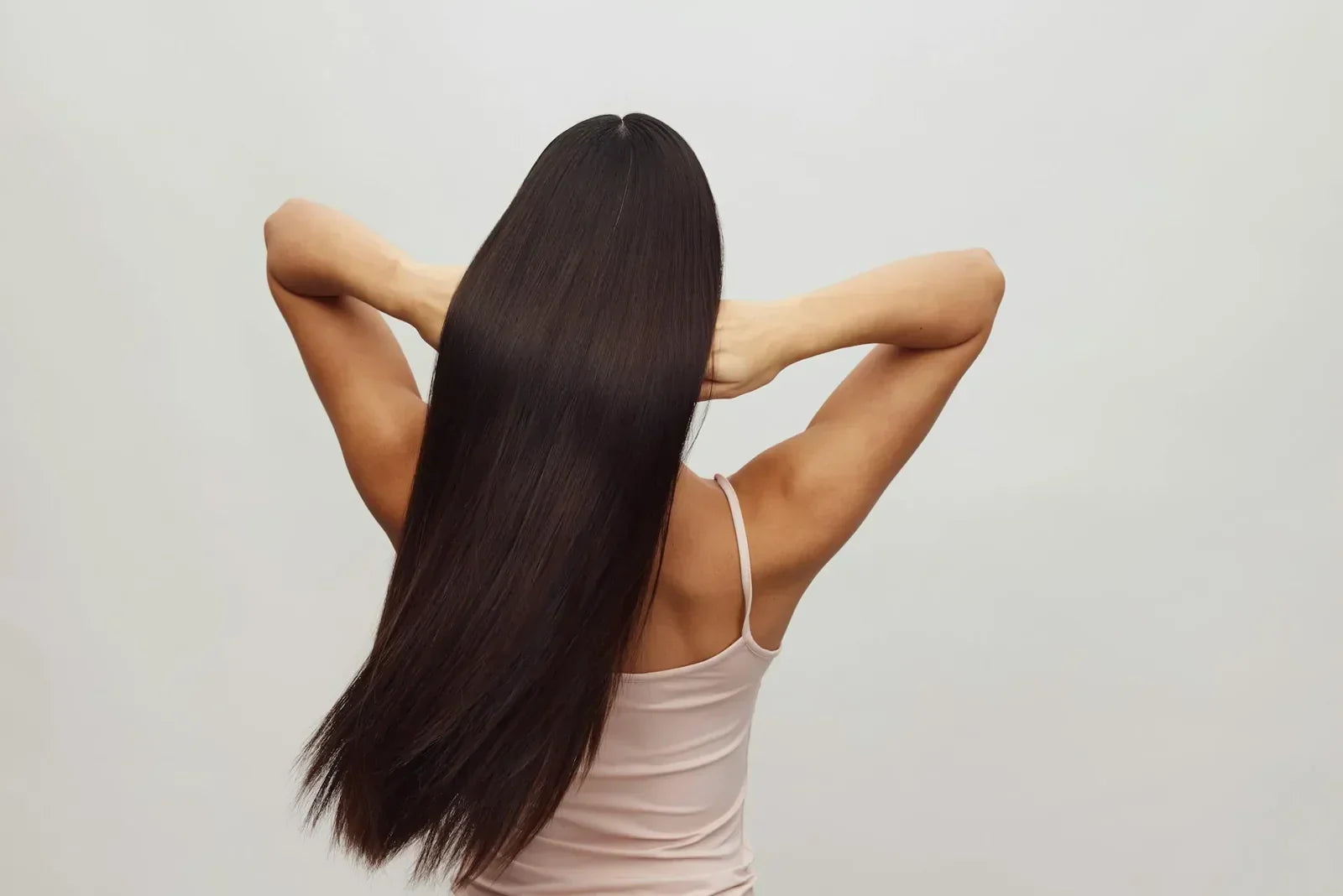 Frau von hinten mit langem, glänzendem dunklen Haar als Symbol für gesunde Haarwurzeln