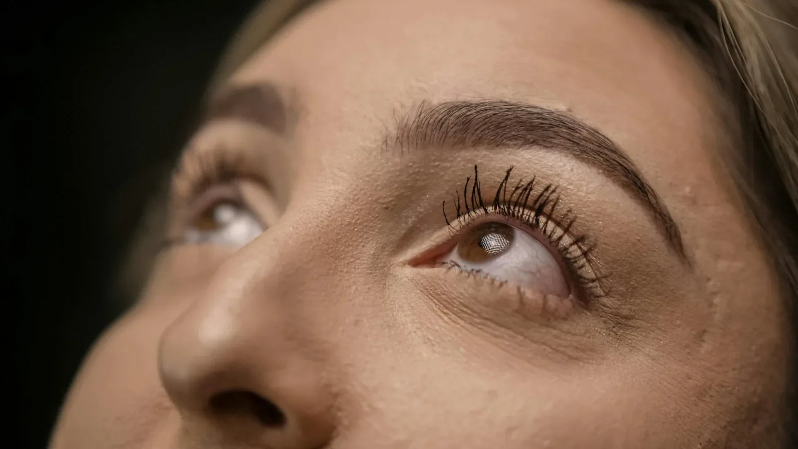 Nahaufnahme eines weiblichen Auges mit dichten, langen Wimpern beim Blick nach oben